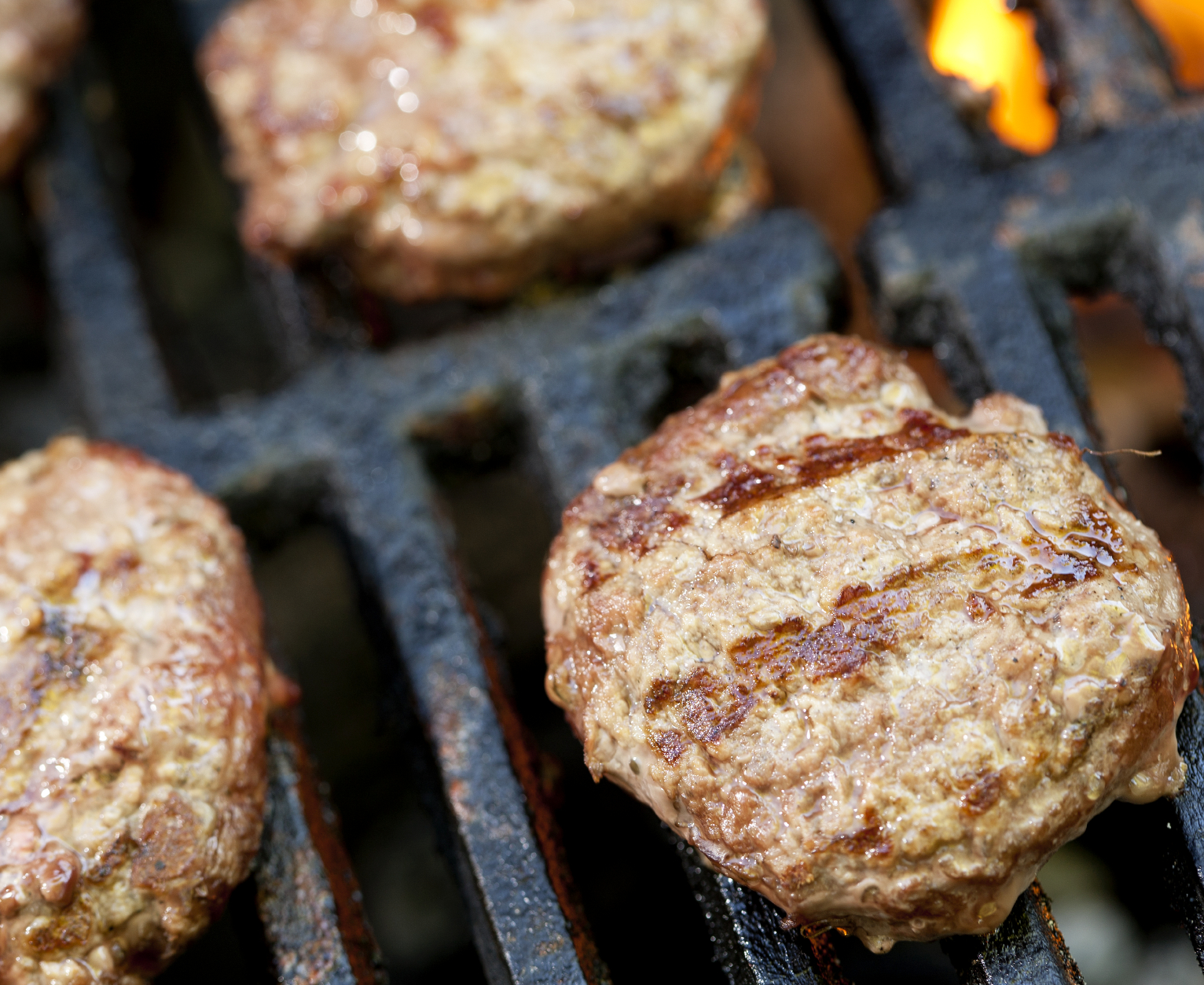 Slider hamburgers cooking on a barbecue grill.